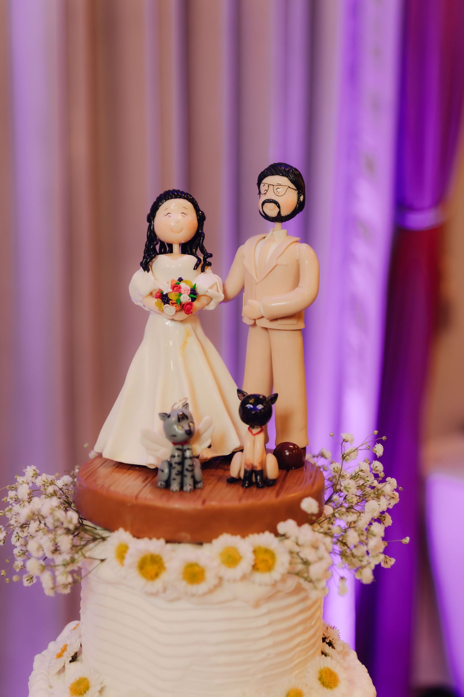 Elegant wedding cake topper featuring custom bride and groom figurines with cats and daisies.