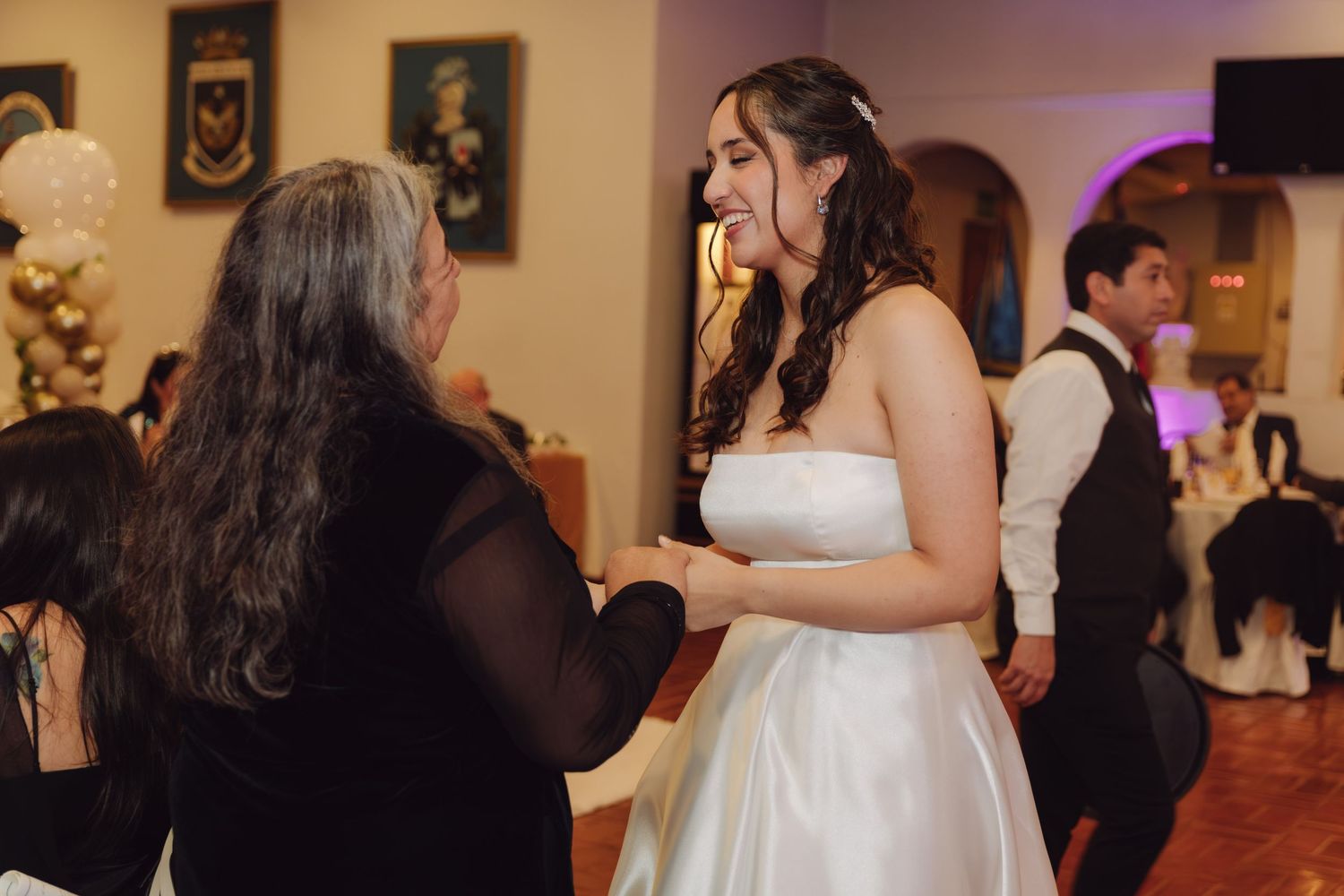 Bride in strapless white gown shares a warm moment with a female guest at the wedding reception.
