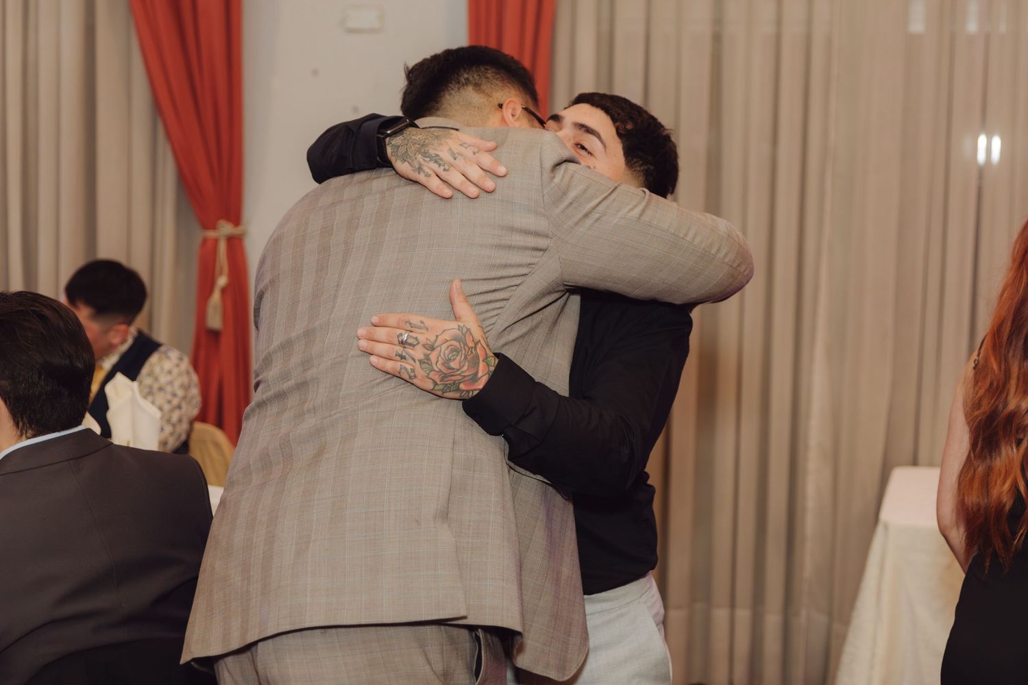 Two men share an emotional hug at a formal wedding reception event.