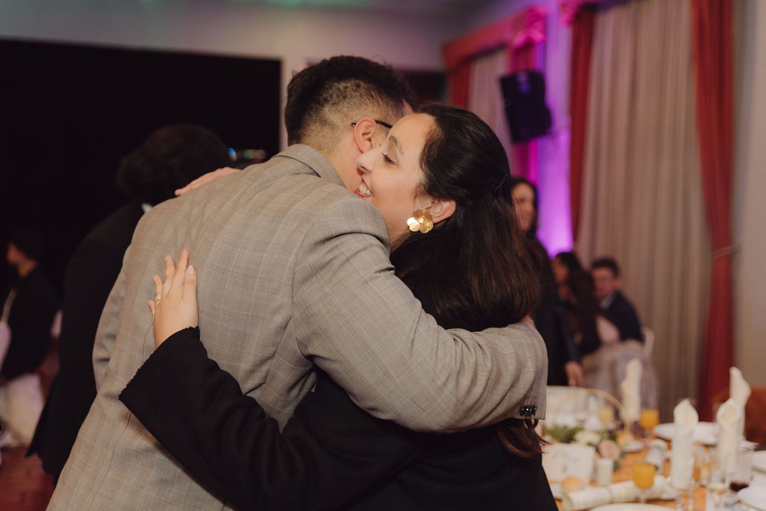 Man in grey suit shares heartfelt hug with older woman at wedding reception.