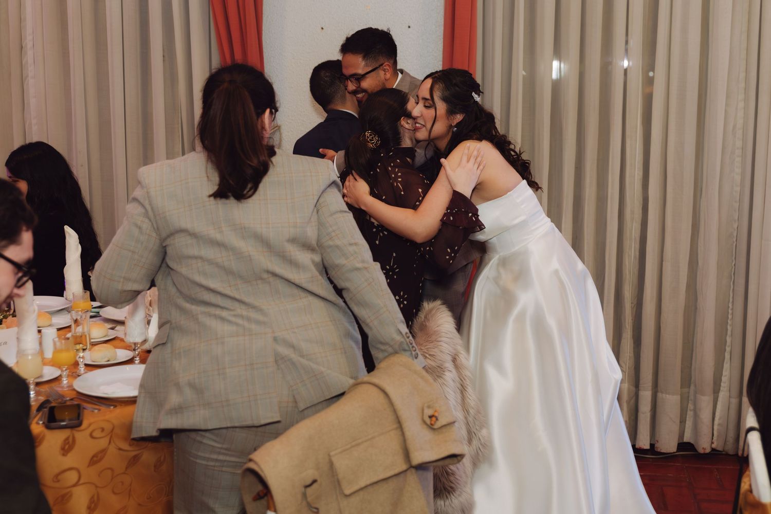 Bride in white gown greets guests with hugs at wedding reception dinner.