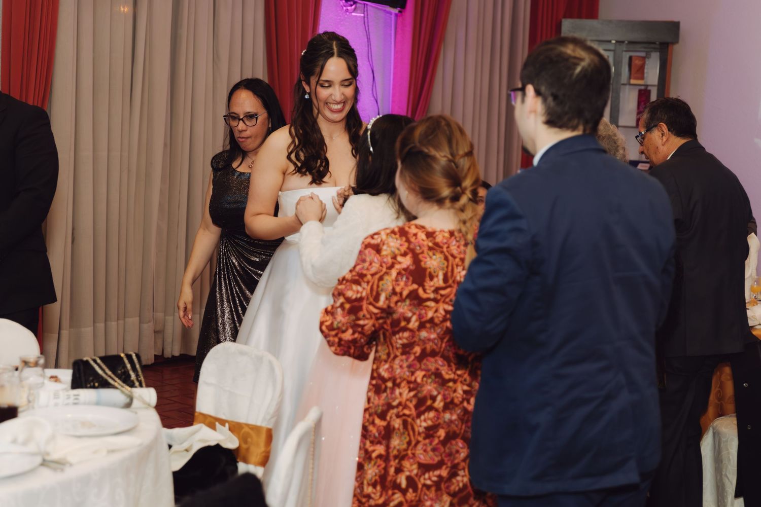 Bride in white gown greets guests warmly at elegant wedding reception.