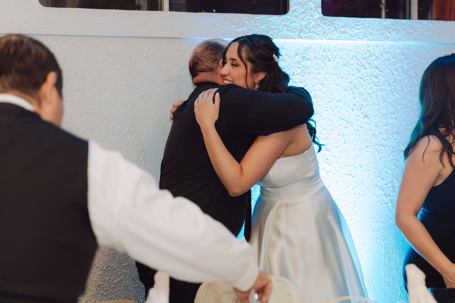 Bride in white gown sharing an emotional hug with a guest at her wedding reception.