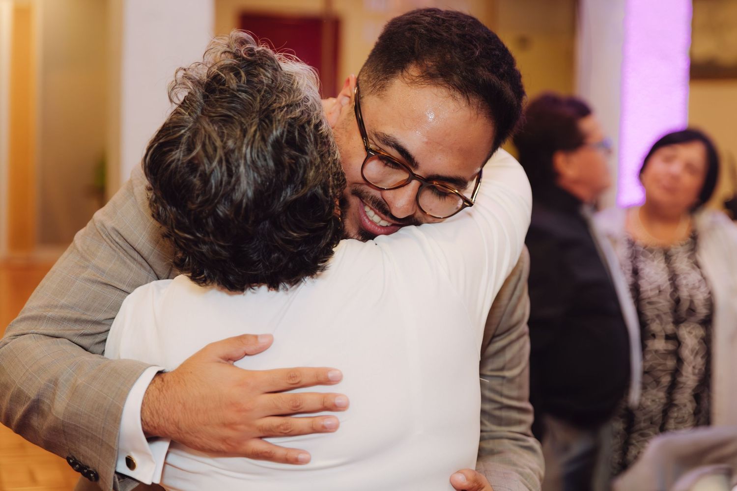 Man in gray suit with glasses sharing a heartfelt hug at a wedding celebration.