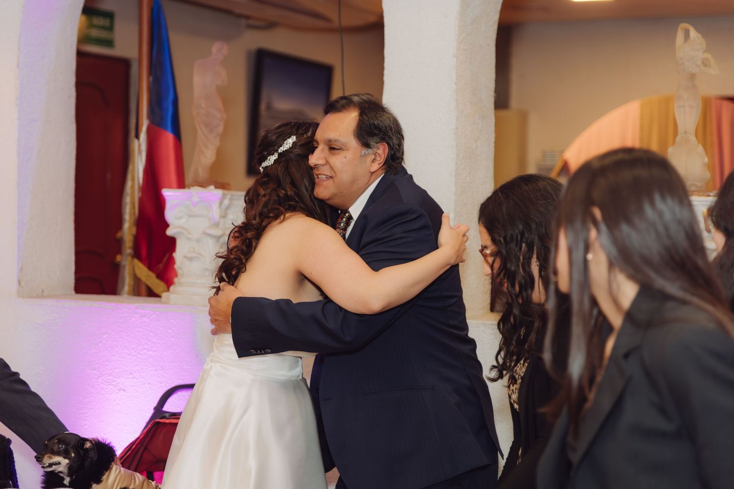 Man in dark suit embracing bride in white wedding dress at reception venue.