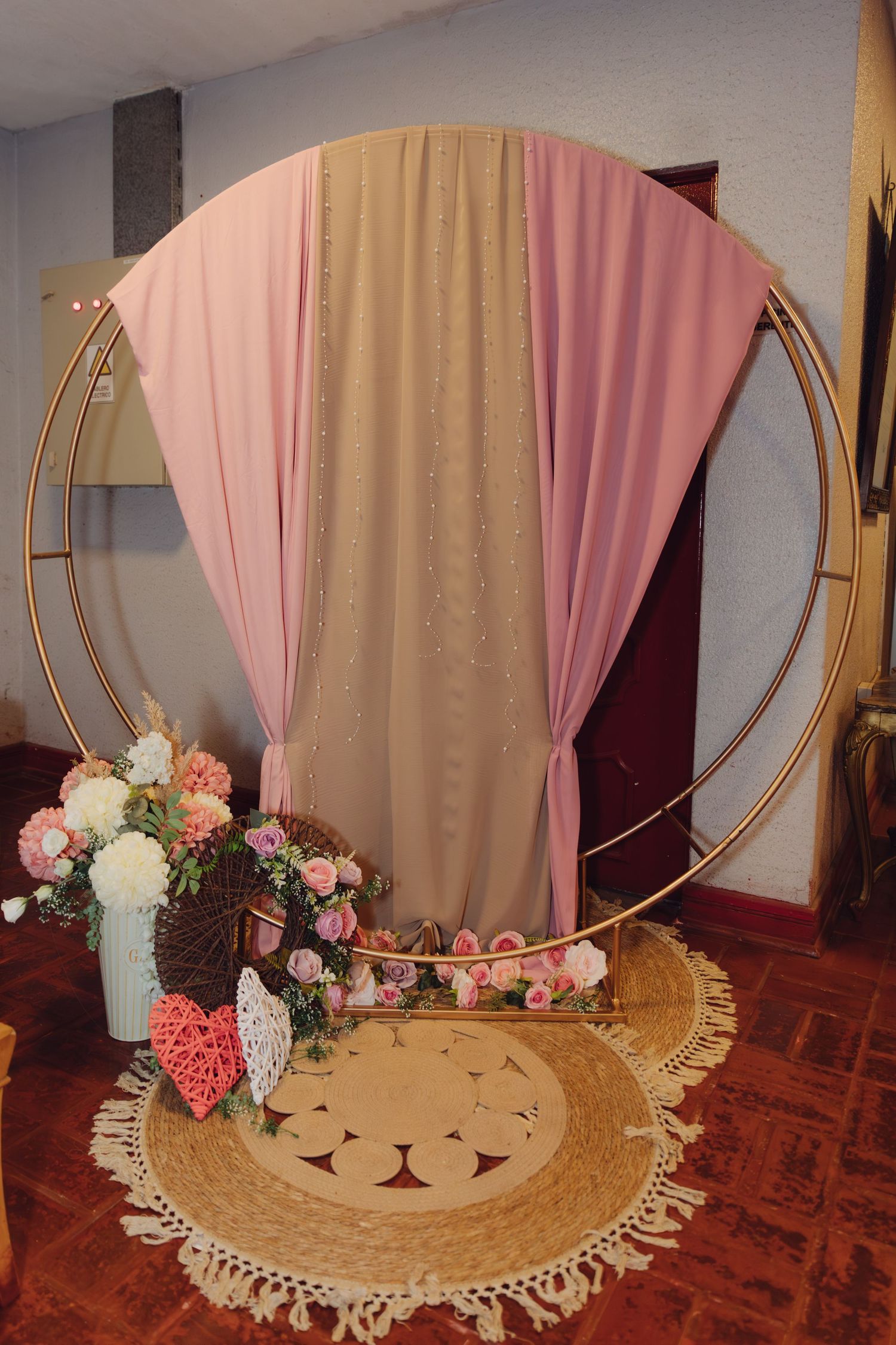 Circular gold arch wedding backdrop with pink and beige draping and floral arrangements.