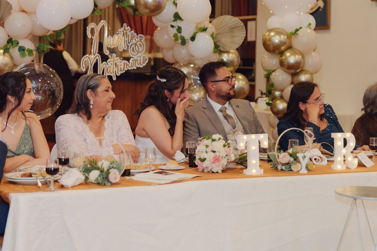 Wedding party seated at decorated head table with balloon arch and Mr and Mrs sign.