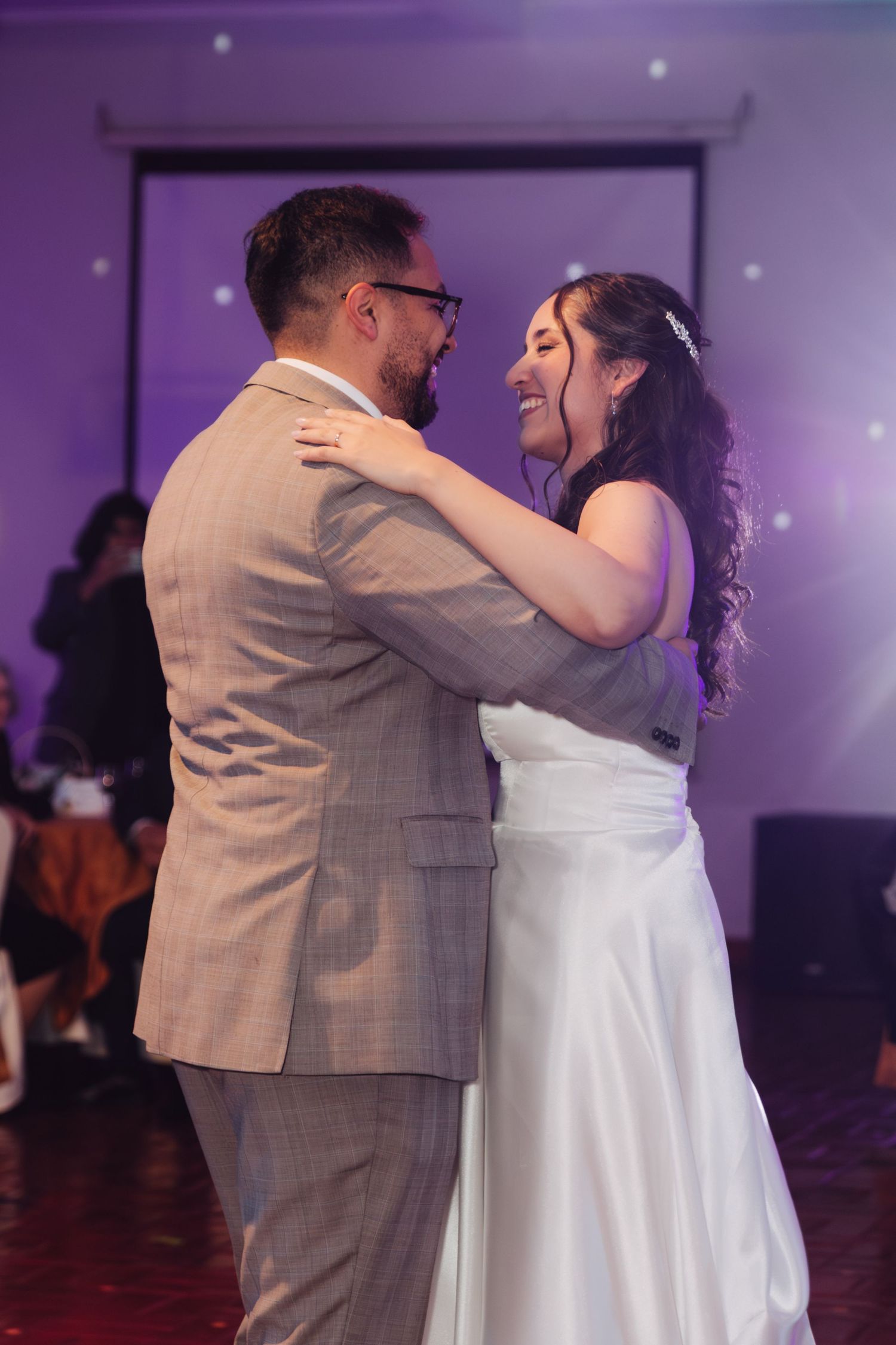 Bride and groom share joyful first dance, bride laughing in white gown at wedding reception.