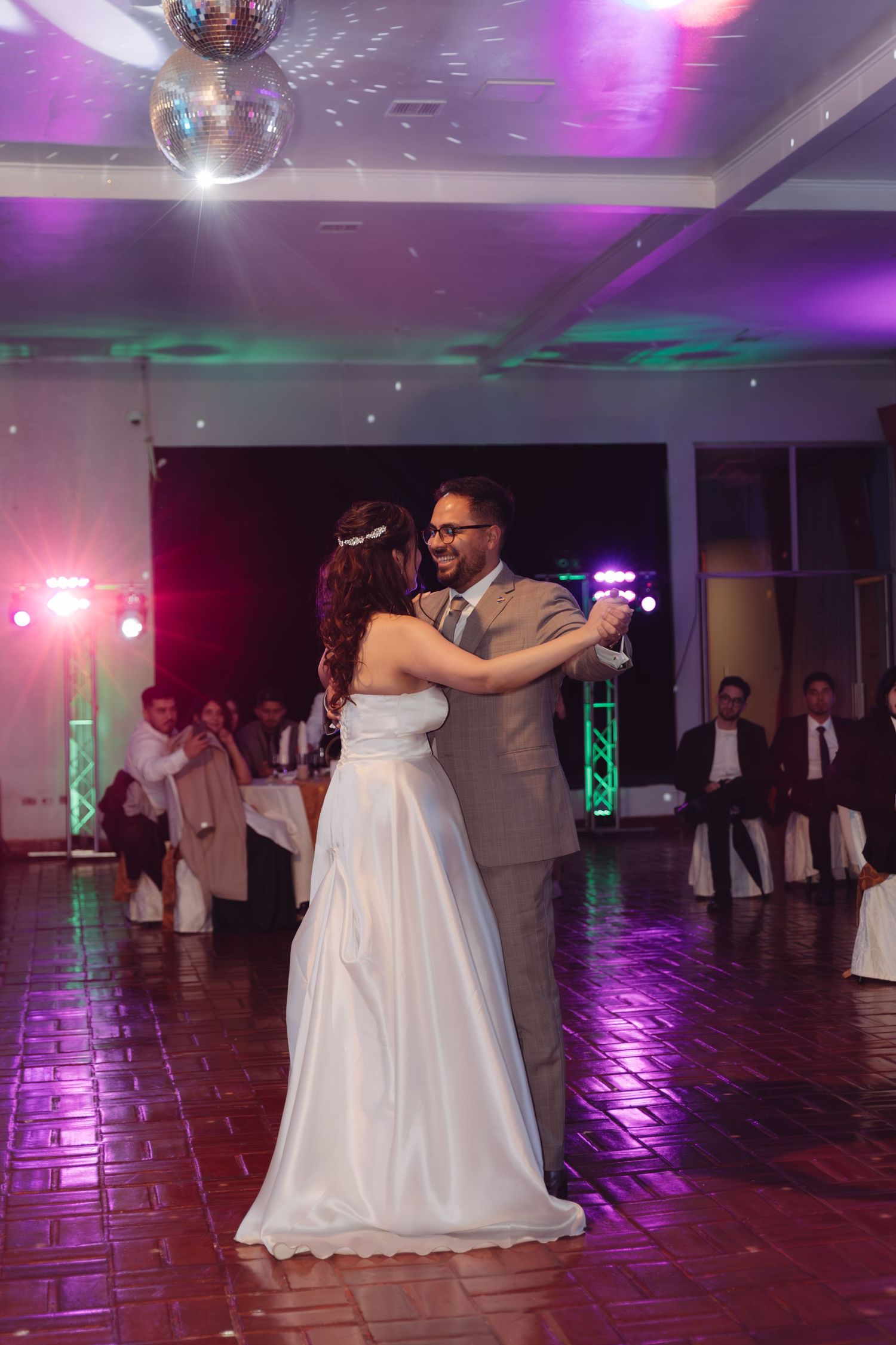 Bride and groom share romantic first dance under disco ball in elegantly lit wedding venue.
