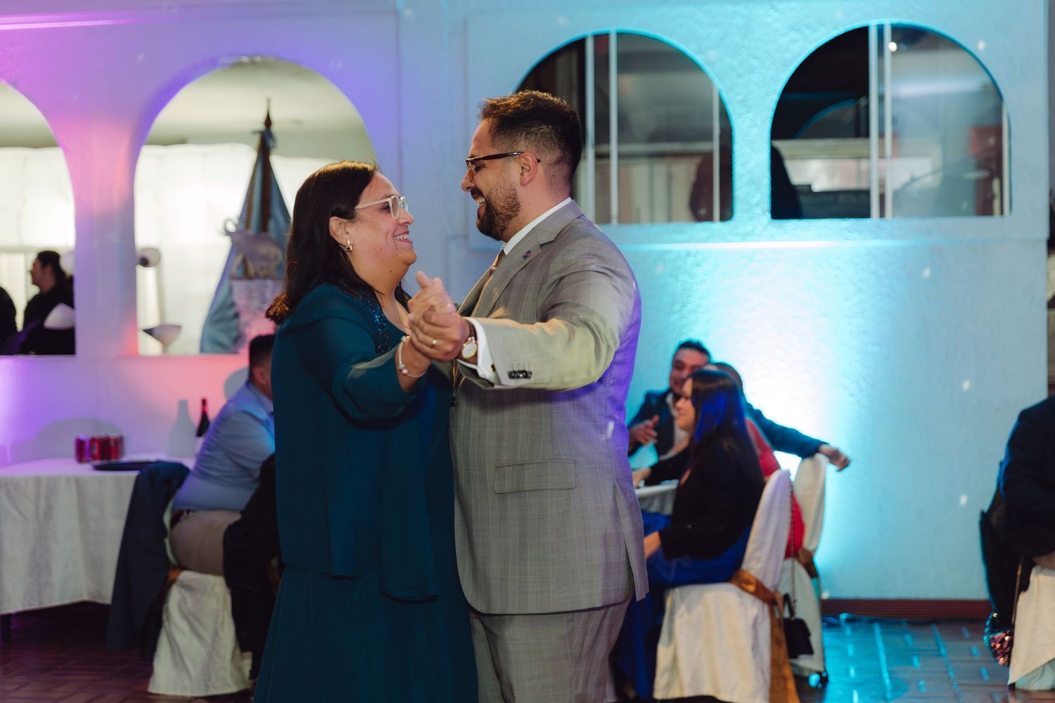 Groom and woman in teal dress share a dance at elegant wedding reception venue.