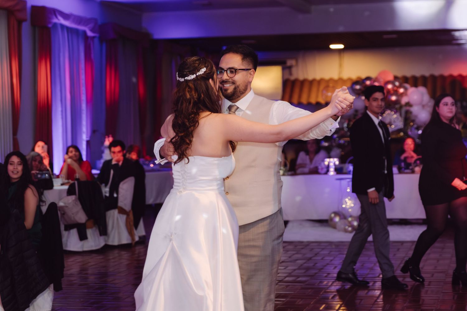 Bride and groom dance together joyfully on the wedding reception dance floor with guests watching.
