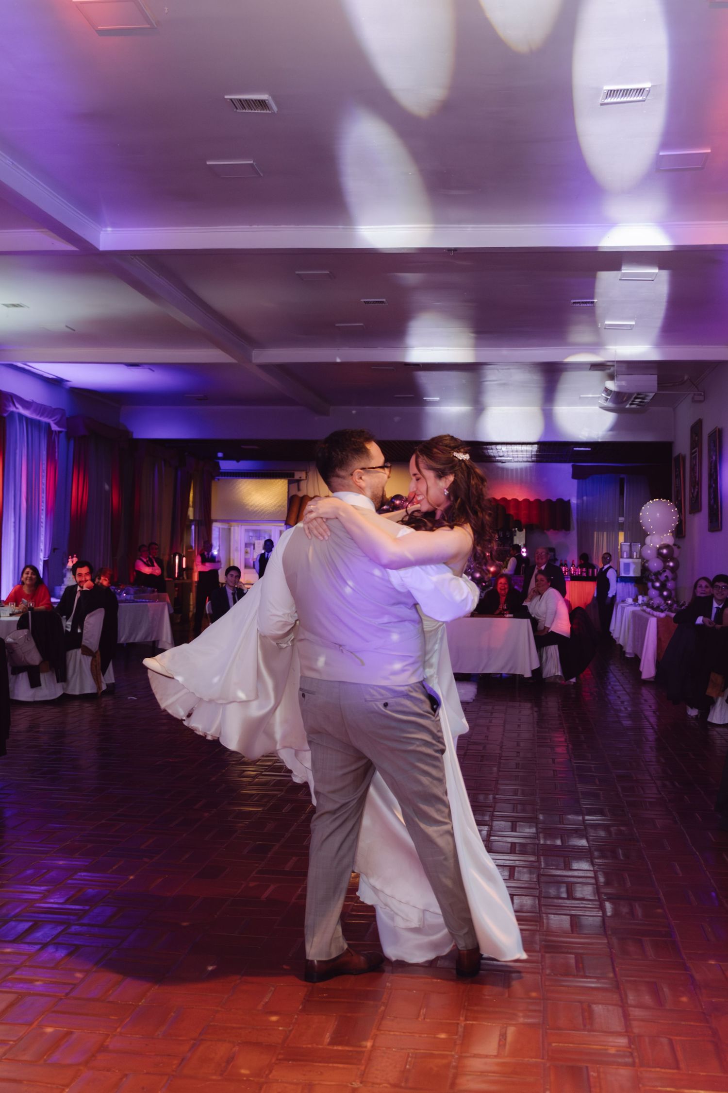 Bride and groom share an intimate embrace during their first dance at a wedding reception with purple lighting.