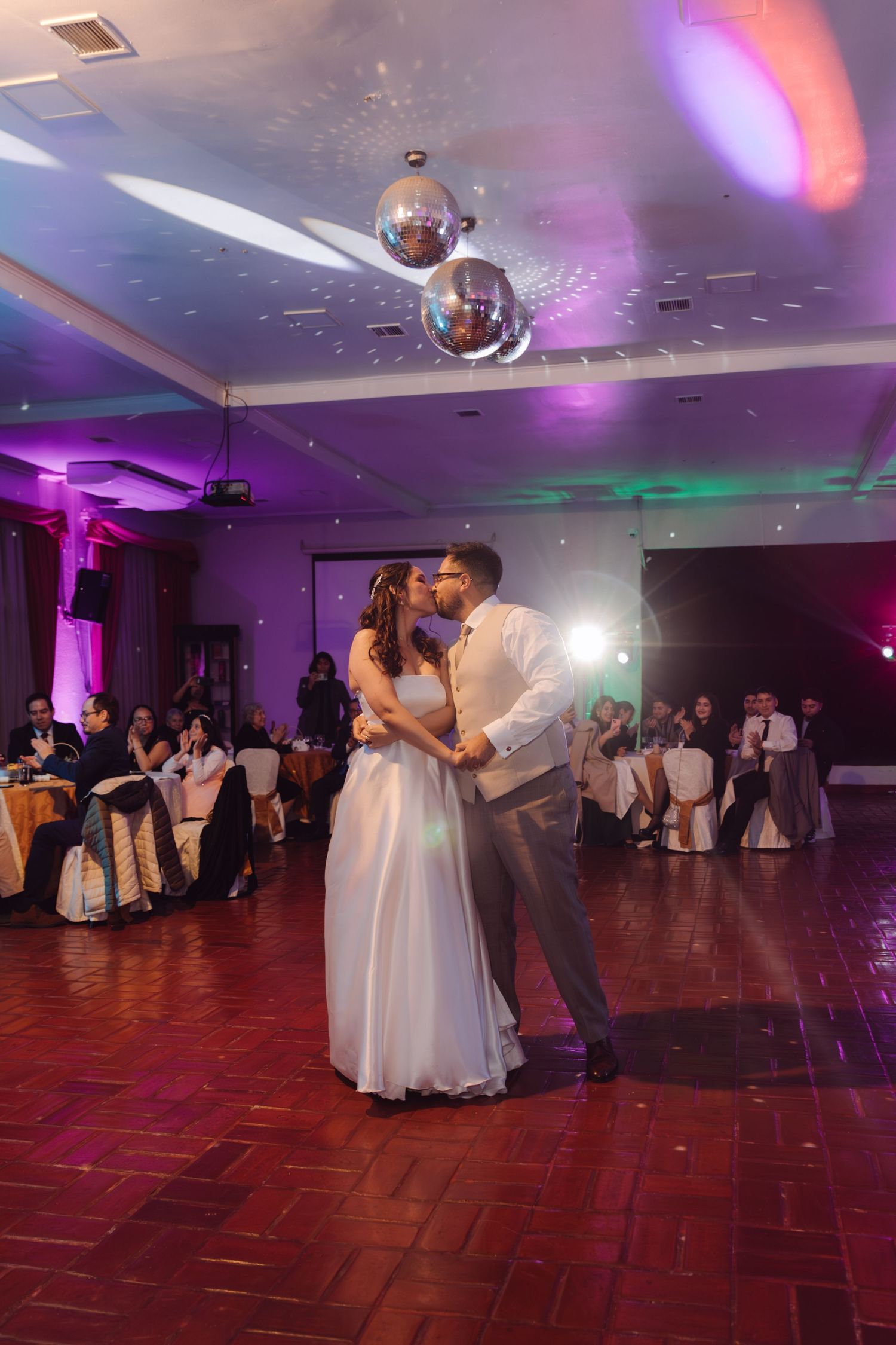 Bride and groom share a kiss during first dance under disco balls at a wedding reception.