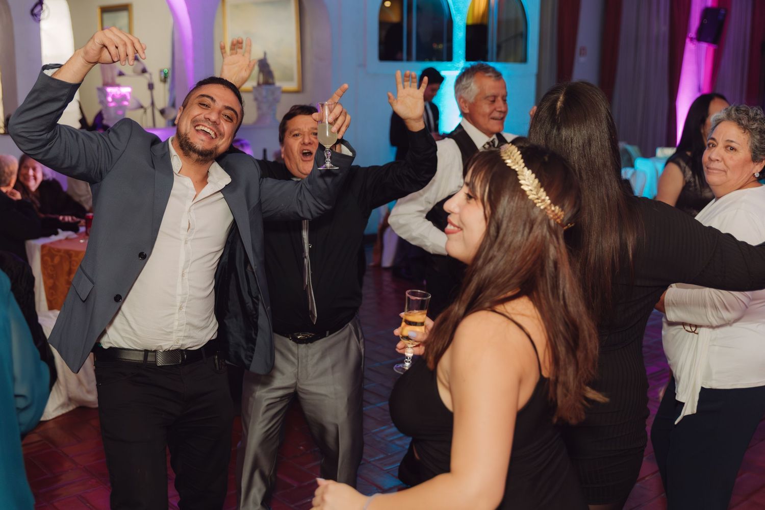 Joyful wedding guests dancing and celebrating with raised arms at a reception.