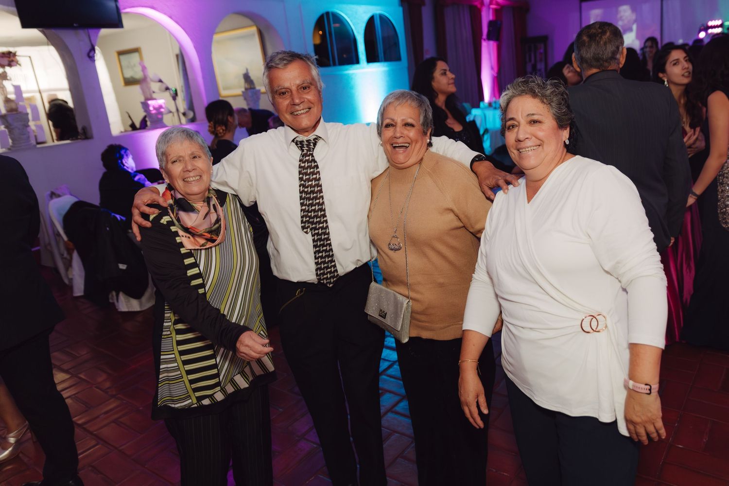 Four smiling guests posing together at a wedding reception with purple lighting.