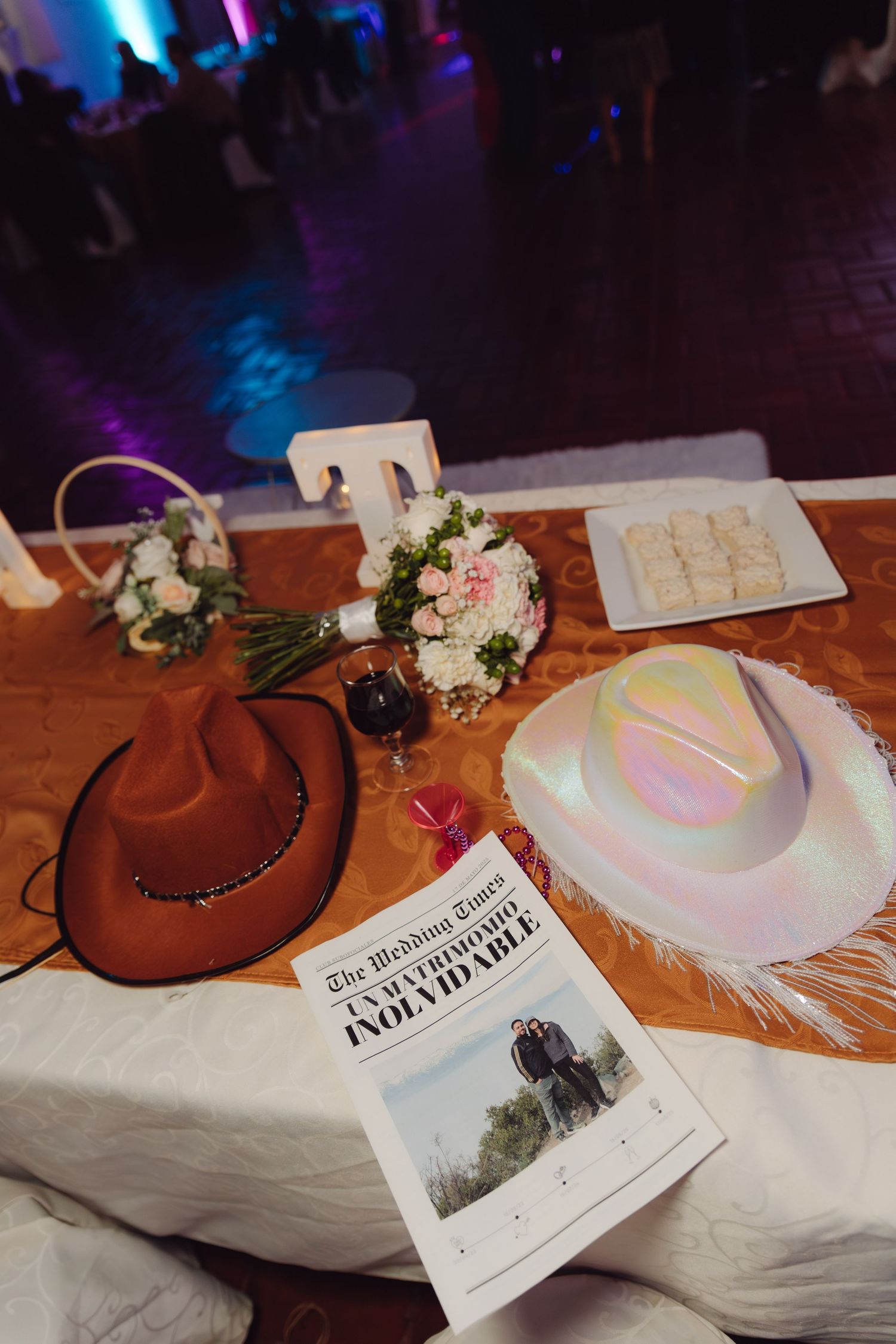 Wedding sweetheart table with cowboy hats, bouquet, and Wedding Times newspaper.