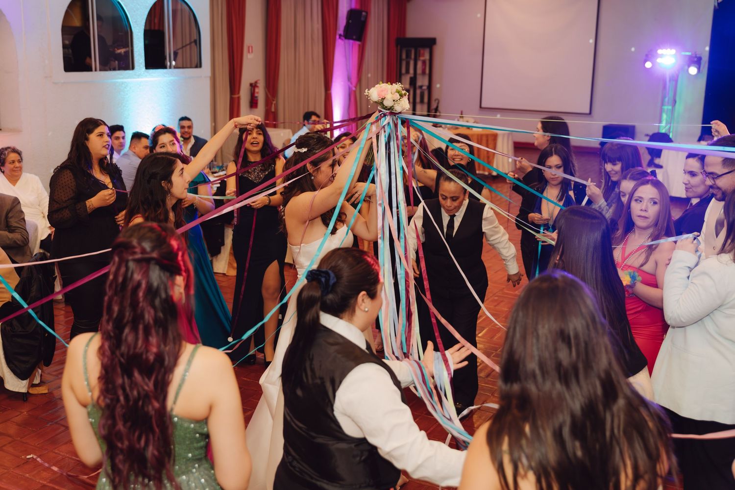 Wedding guests holding colorful ribbons over bride and groom in fun tradition.