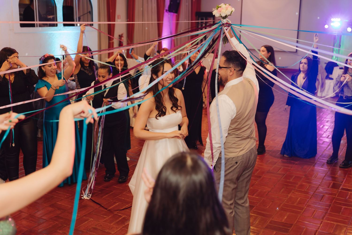 Bride and groom surrounded by colorful streaming ribbons held by wedding guests.