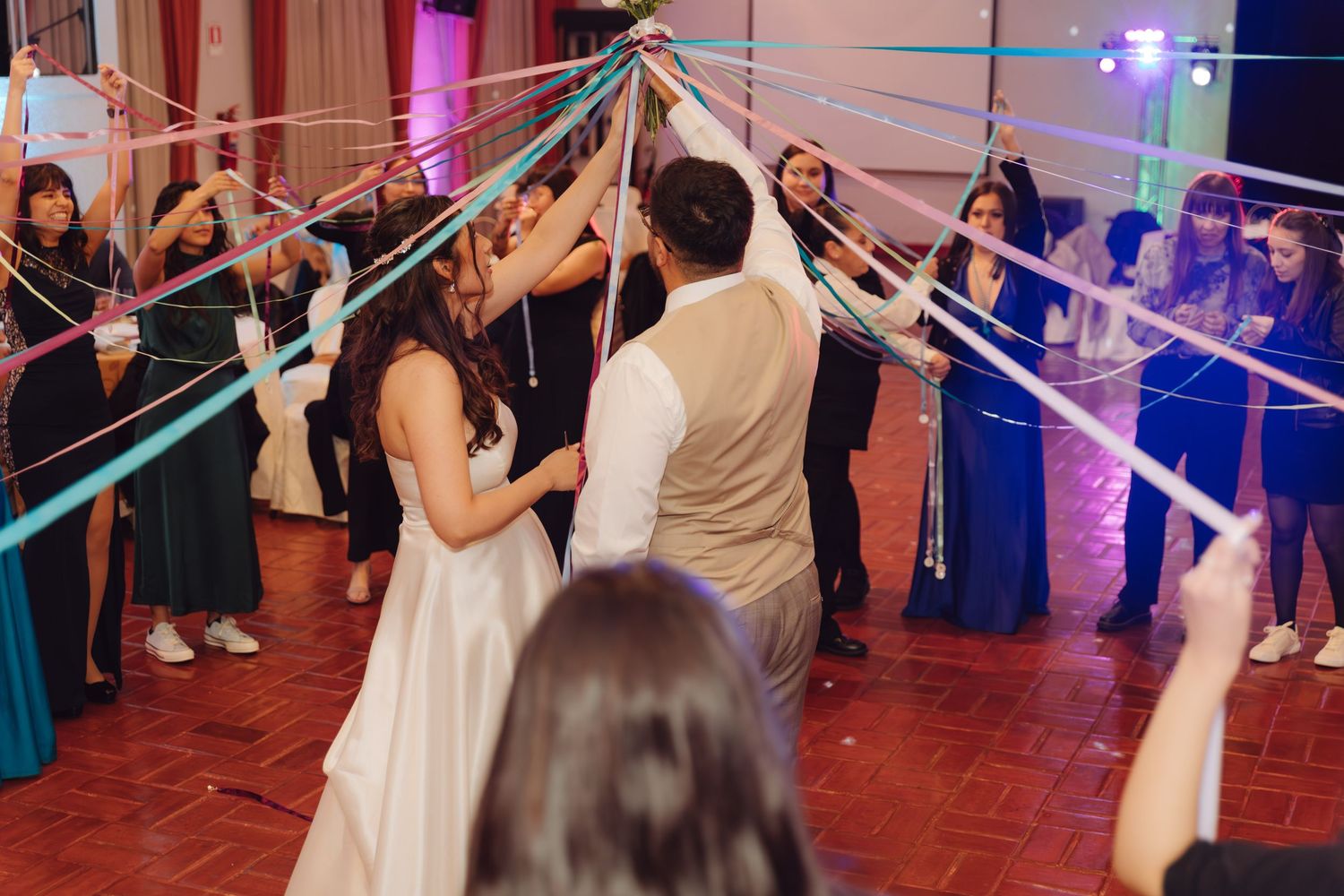 Bride and groom sharing a kiss under colorful ribbons at wedding reception.