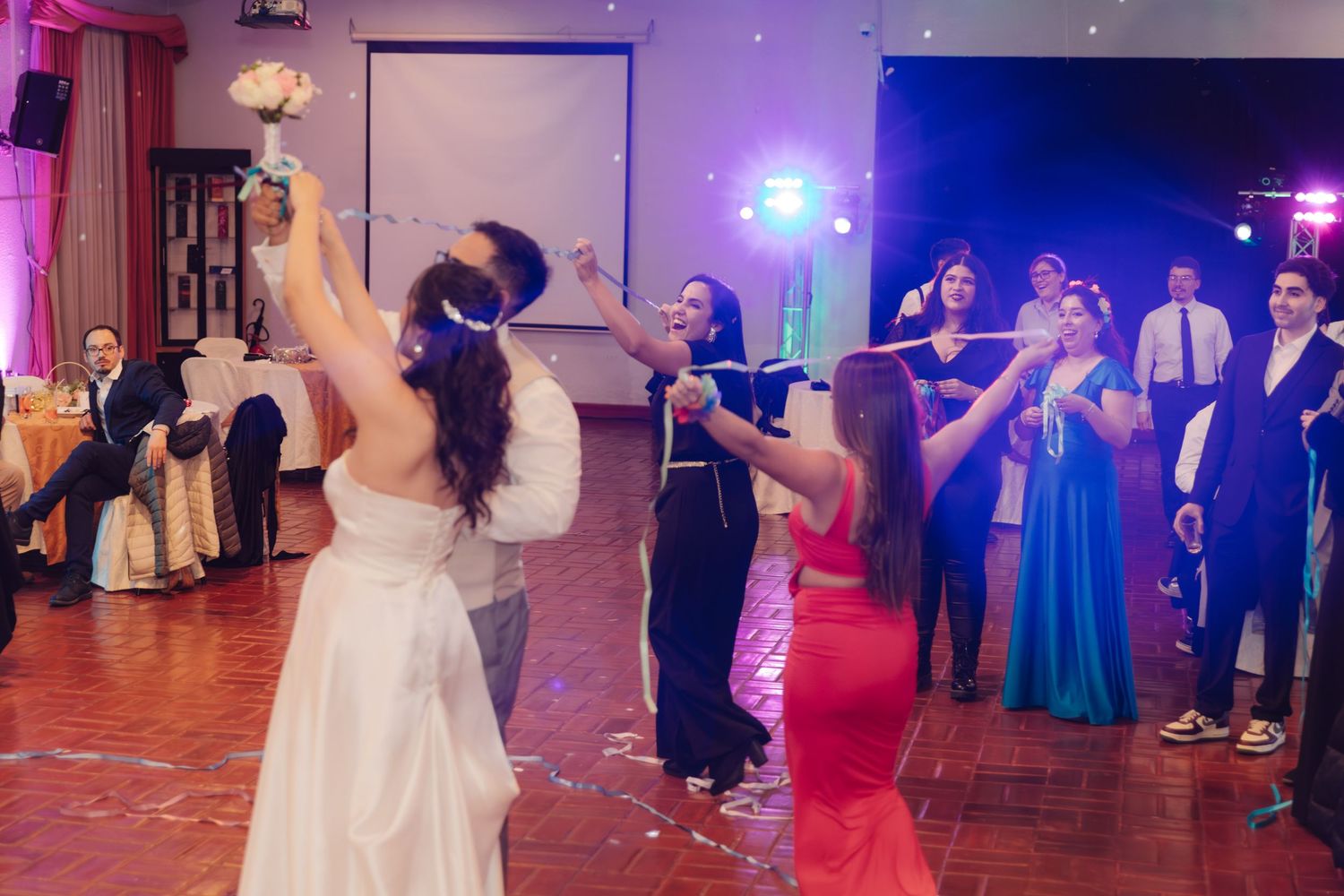 Bride in white gown holds bouquet with colorful ribbons shared with guests at wedding.