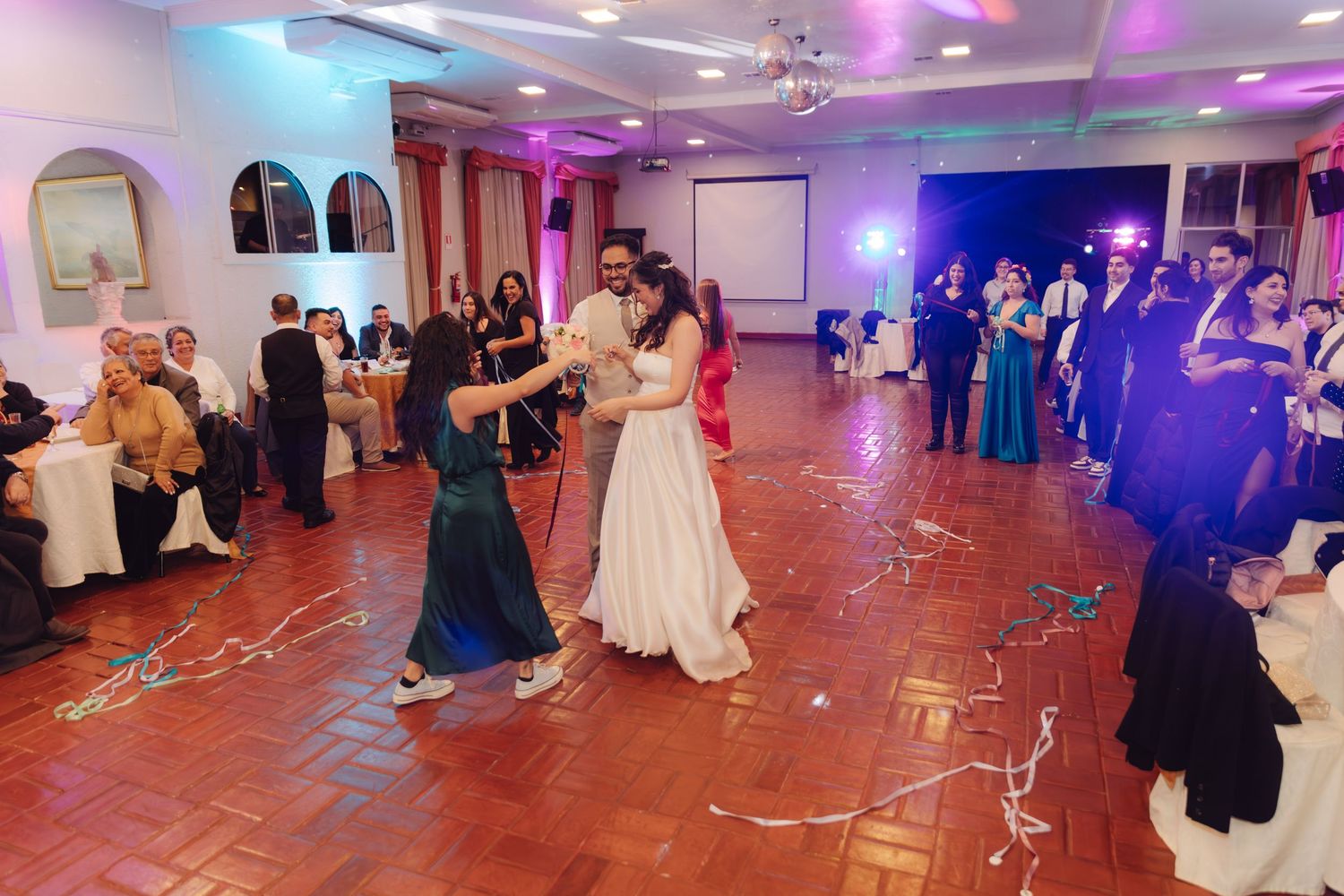 Bride and groom share first dance on terracotta floor surrounded by seated wedding guests.