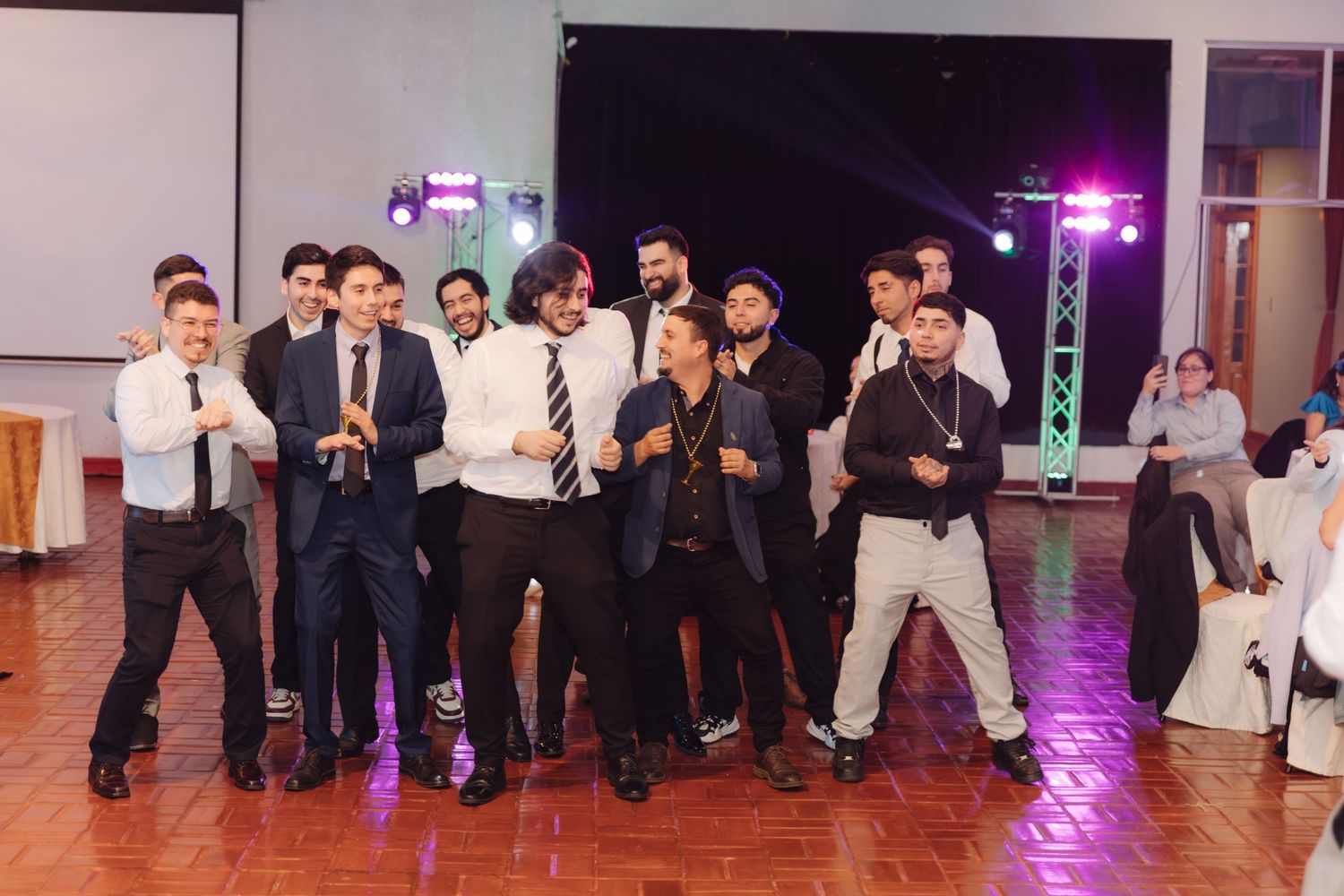 Group of well-dressed men strike fun poses together on wedding reception dance floor.