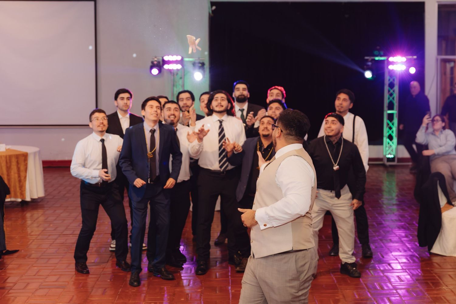 Excited group of men look up anticipating garter toss at lively wedding reception.