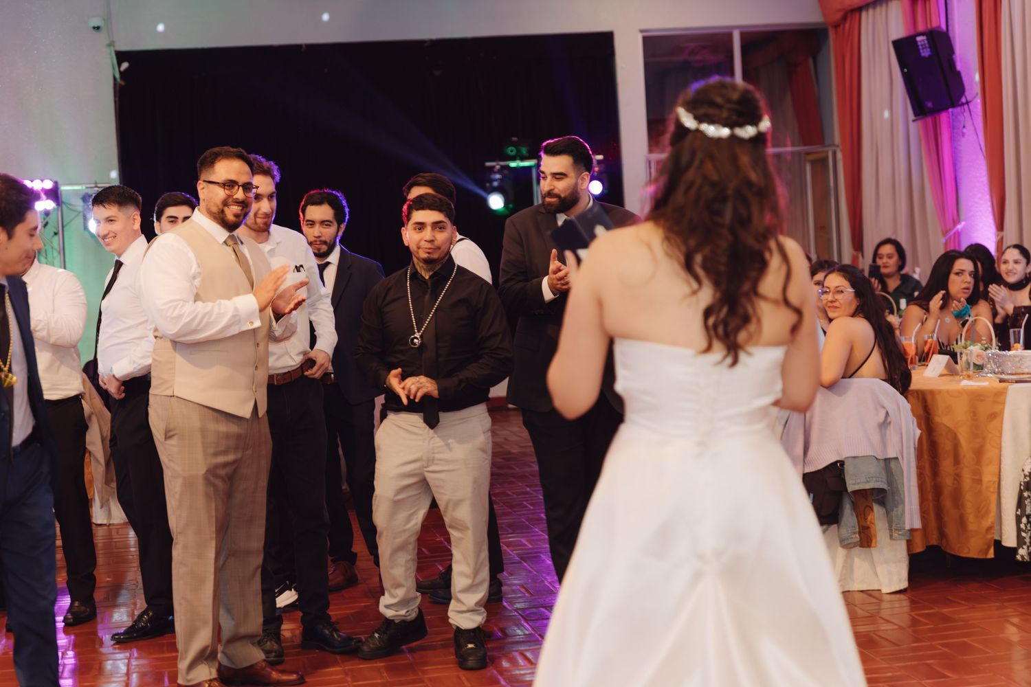 Bride in white gown facing wedding guests during reception dance at elegant venue.