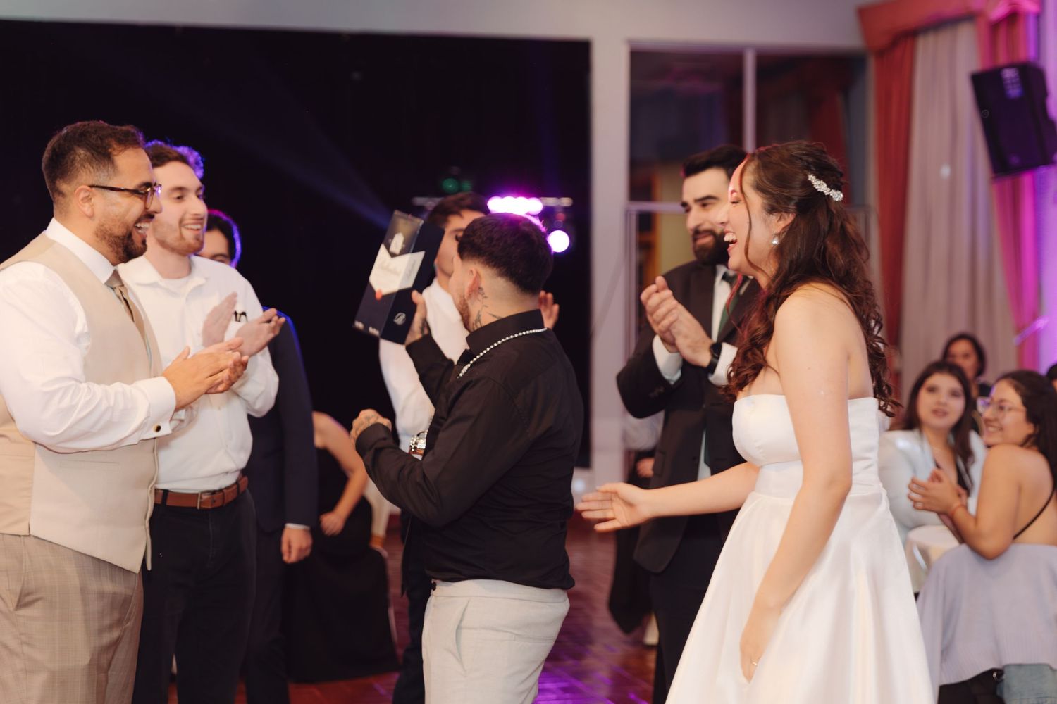 Bride and groom sharing a joyful dance moment with smiling guests at wedding reception.