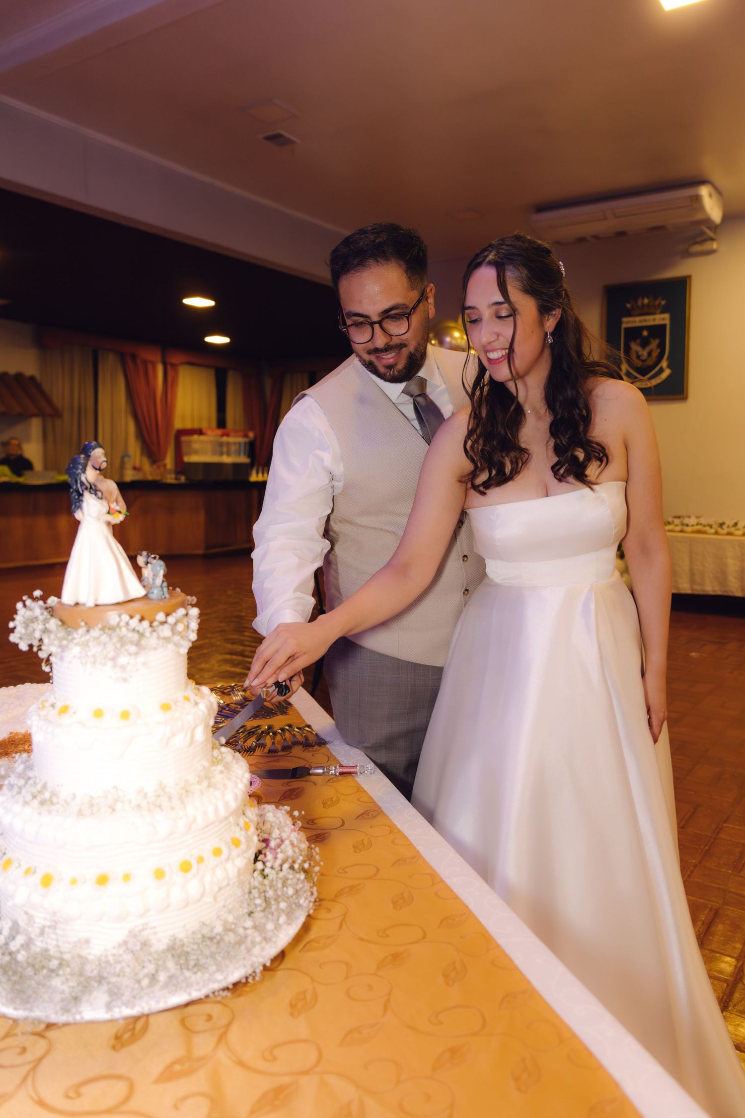 Newlyweds cutting their white three-tier wedding cake decorated with flowers and figurines.