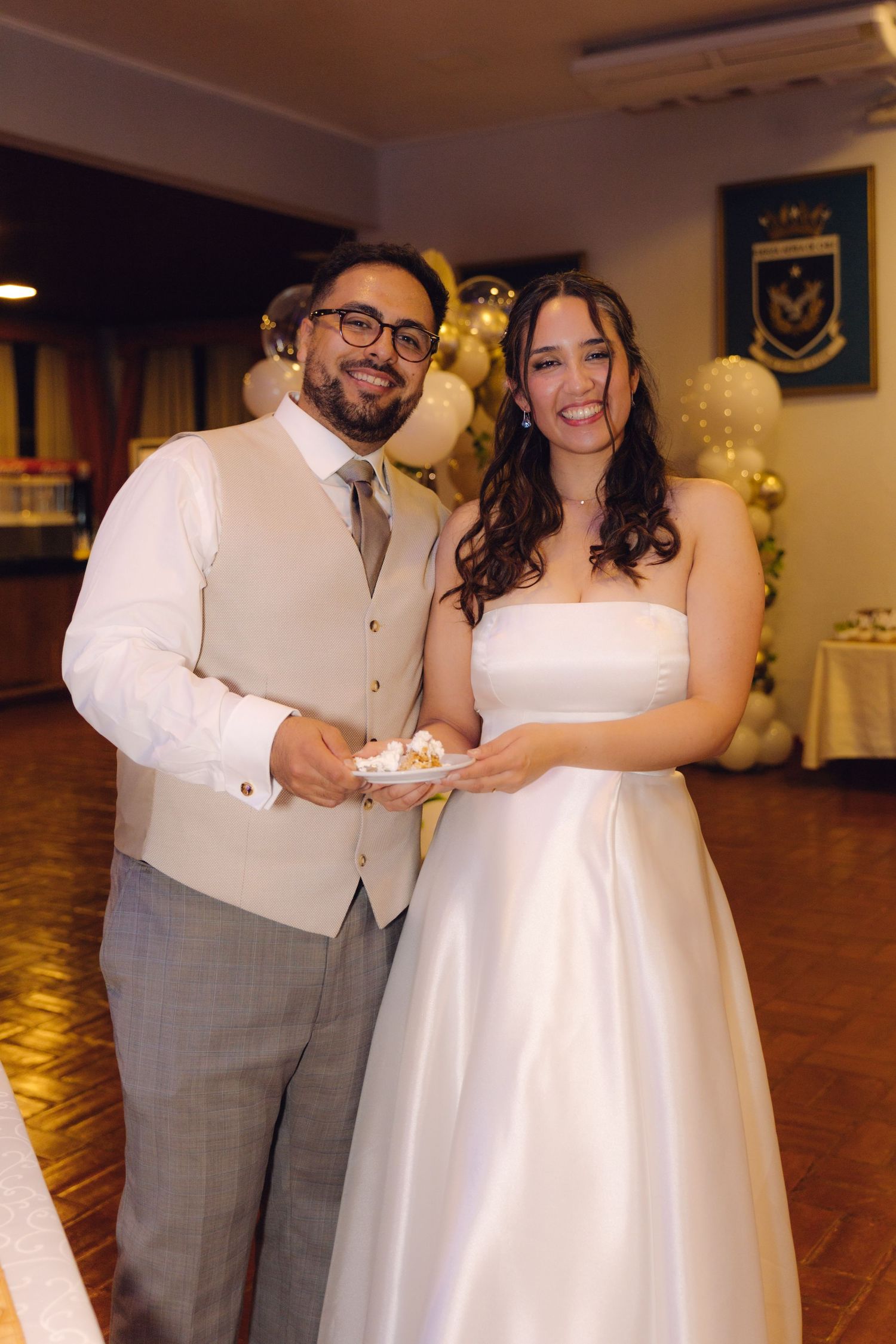 Smiling bride and groom posing together holding cake slices at their wedding reception.