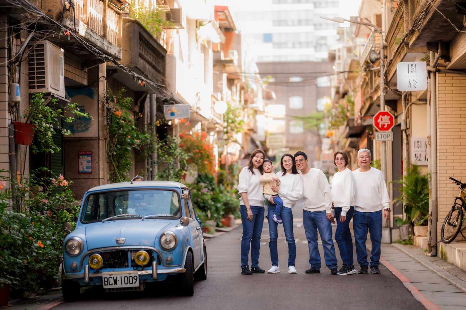A vintage blue car parked on a charming narrow street with potted plants and balconies in an old Mediterranean town.