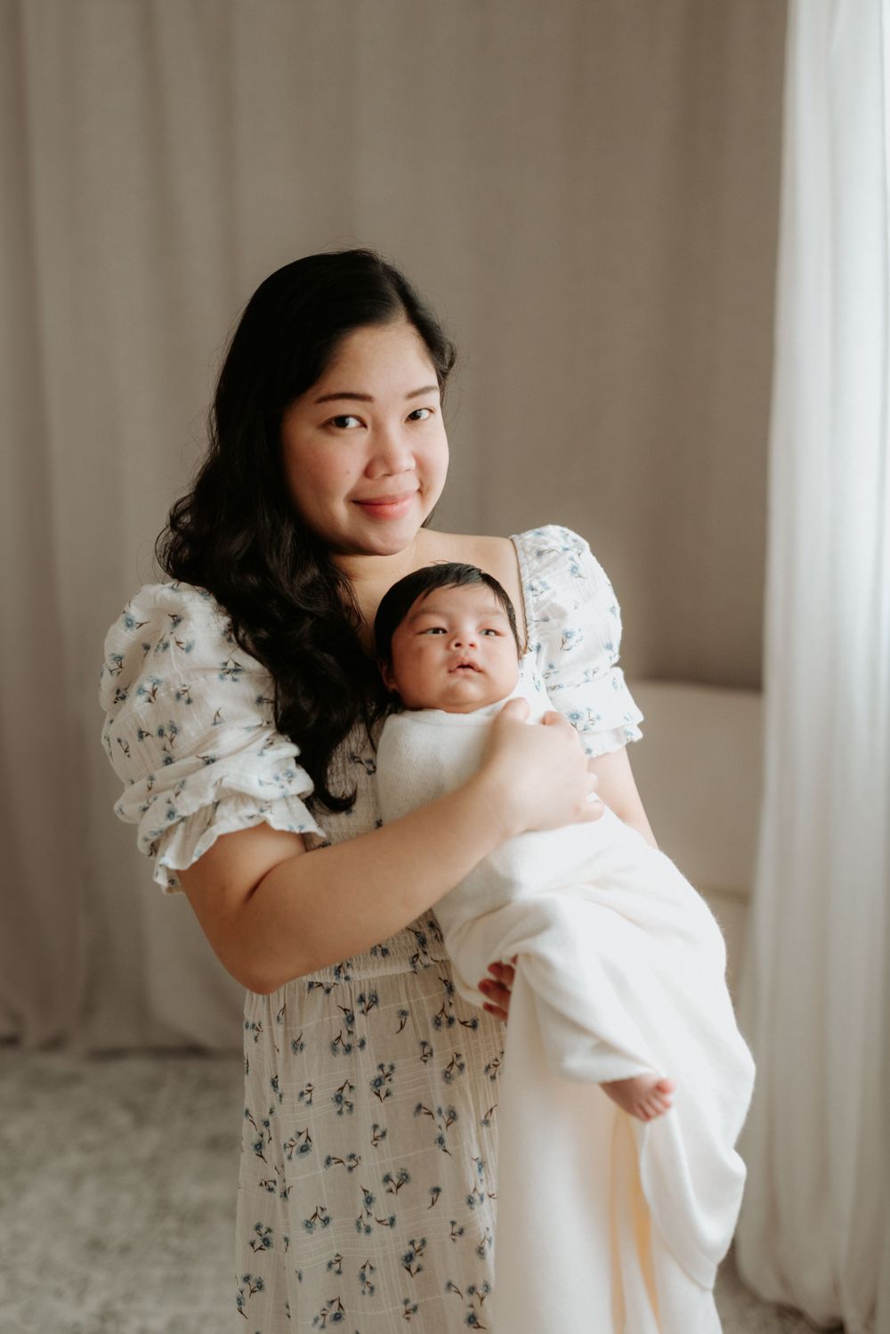 A tender moment between parent and infant in a floral dress against neutral backdrop.