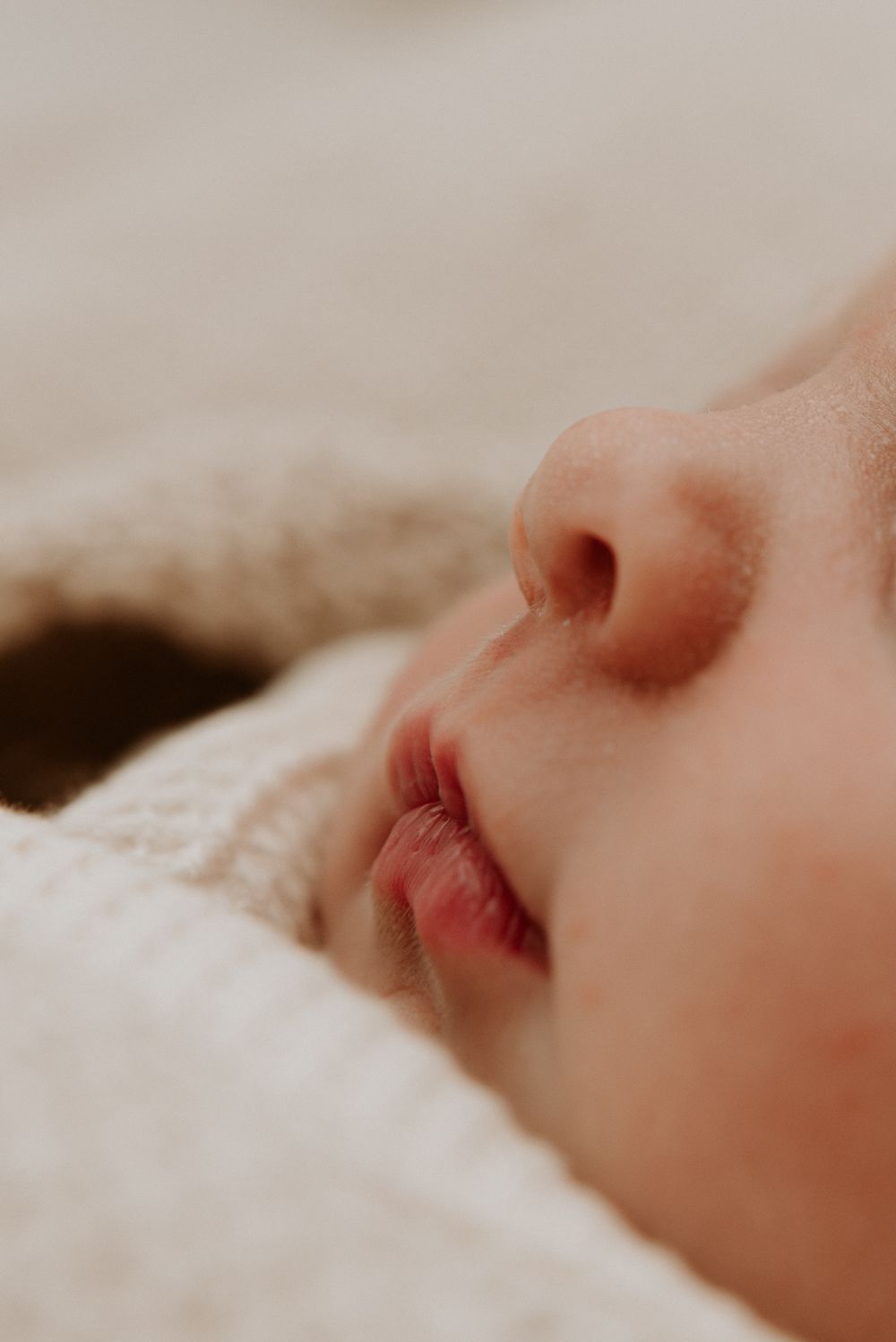 Close-up of a sleeping newborn baby's nose and lips wrapped in a soft white knit blanket.