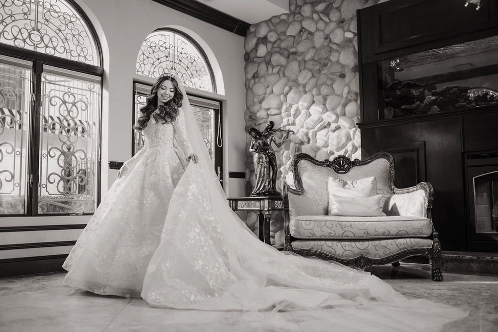 A stunning bridal gown with a long train is displayed in an ornate room with stone walls.