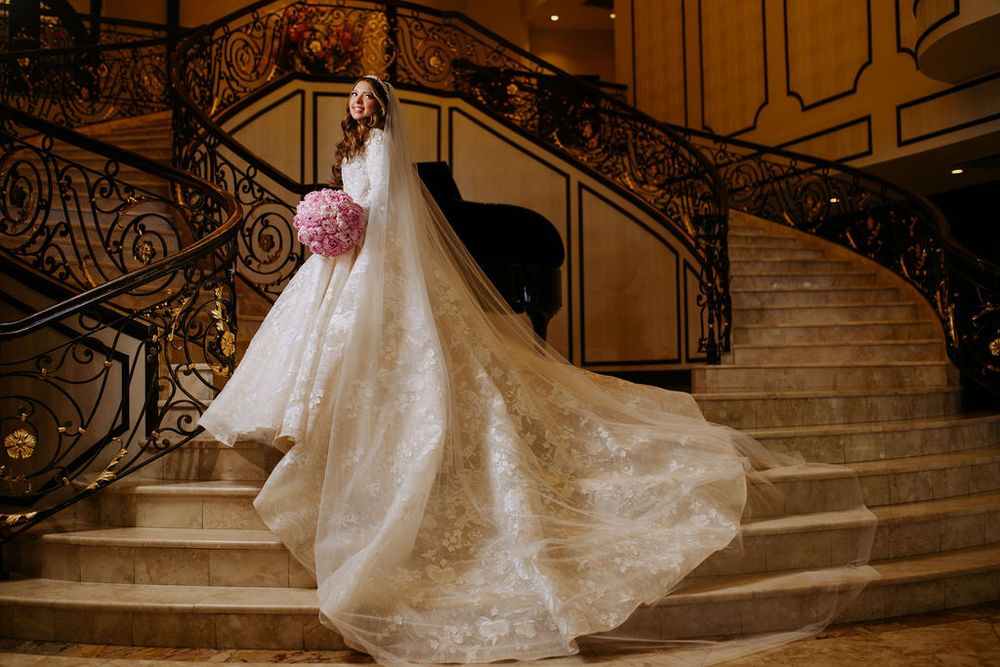 A stunning wedding dress with a long flowing train displayed on an elegant grand staircase with ornate railings.