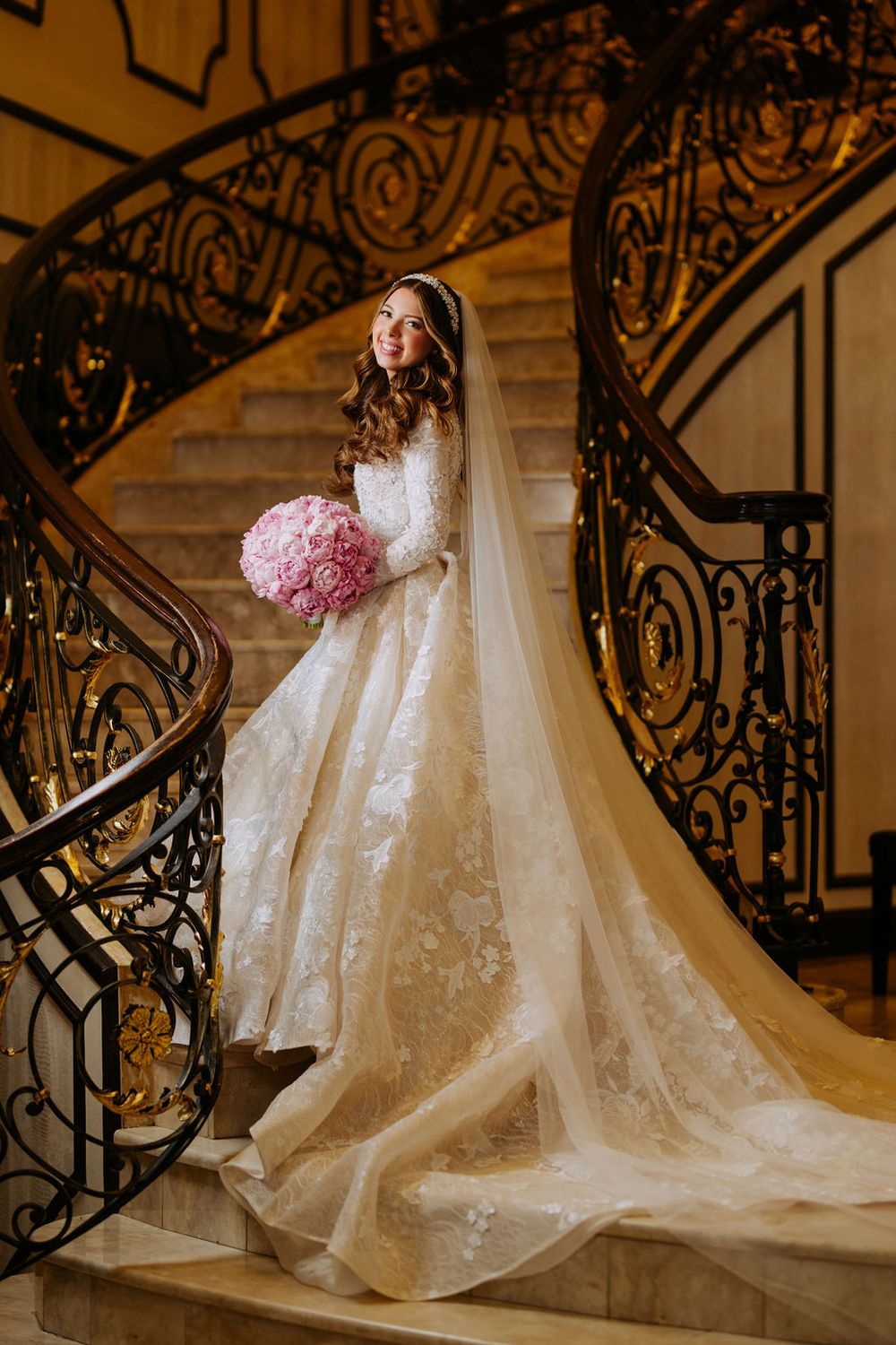 A dramatic wedding dress with lace details cascades down ornate stairs with intricate iron railings.