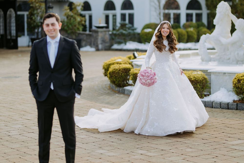 Elegant wedding couple poses in front of white architectural columns and arches.