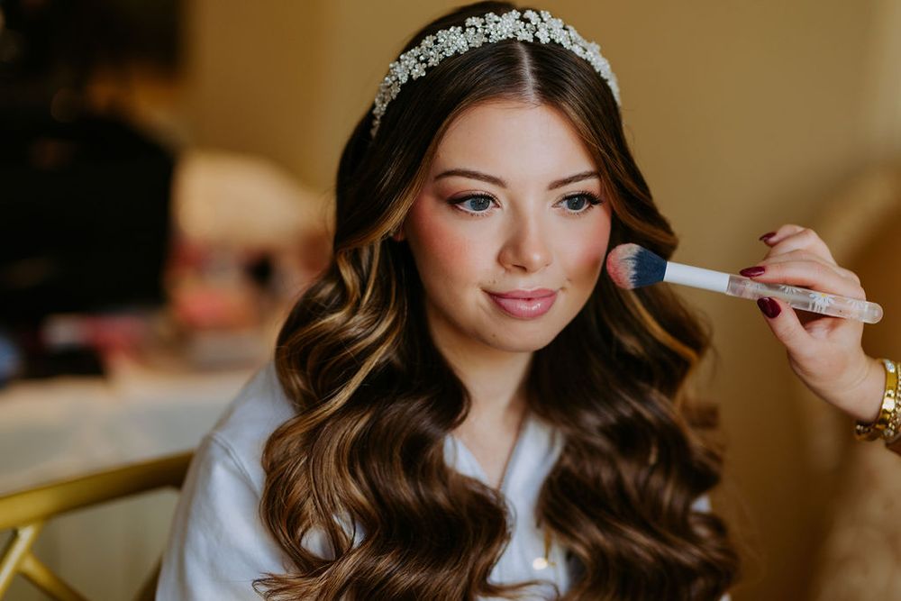 Makeup artist applies finishing touches to bride's hair and makeup during wedding preparations.