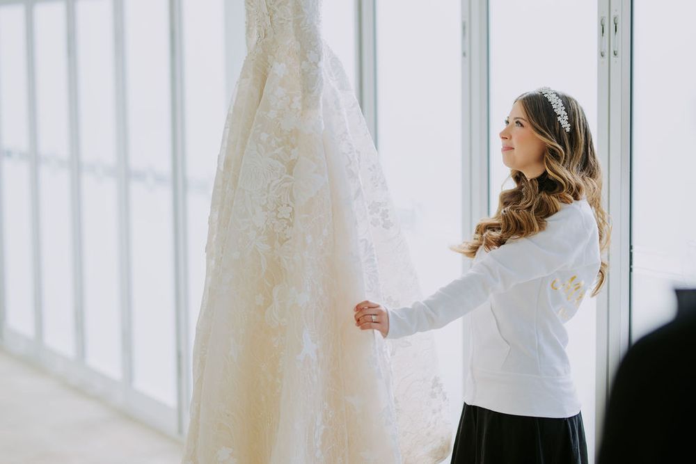 Elegant white wedding dress displayed in bright sunlit room with large windows.