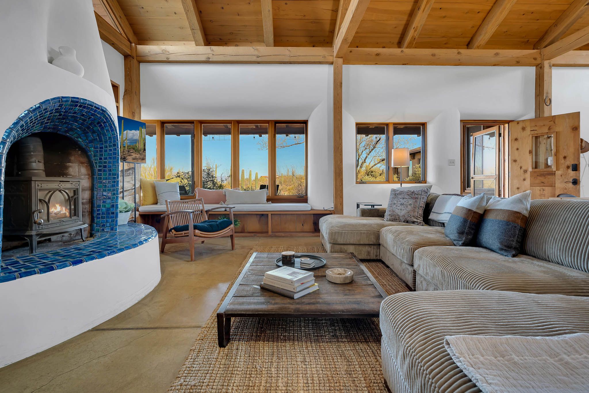 Modern living room with blue adobe fireplace, gray sectional sofa, and large windows overlooking desert landscape.