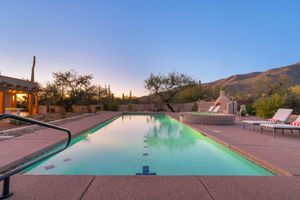 Luxurious infinity pool overlooking desert landscape at sunset with mountain views and lounge chairs.
