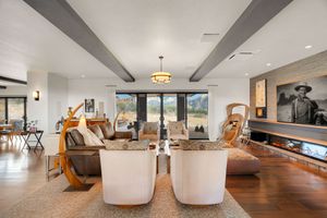 Contemporary open concept living space with exposed beams, white chairs, and hardwood flooring.