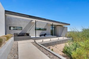 Modern desert home with sleek angular architecture features white walls and expansive windows against a bright blue sky.