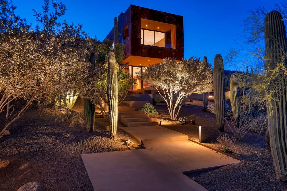 Modern desert home illuminated at dusk with saguaro cacti and landscape lighting creating a warm southwestern ambiance.
