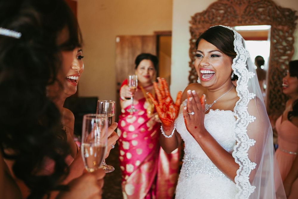 A bride in a white lace gown laughs joyfully while getting ready with her bridal party.
