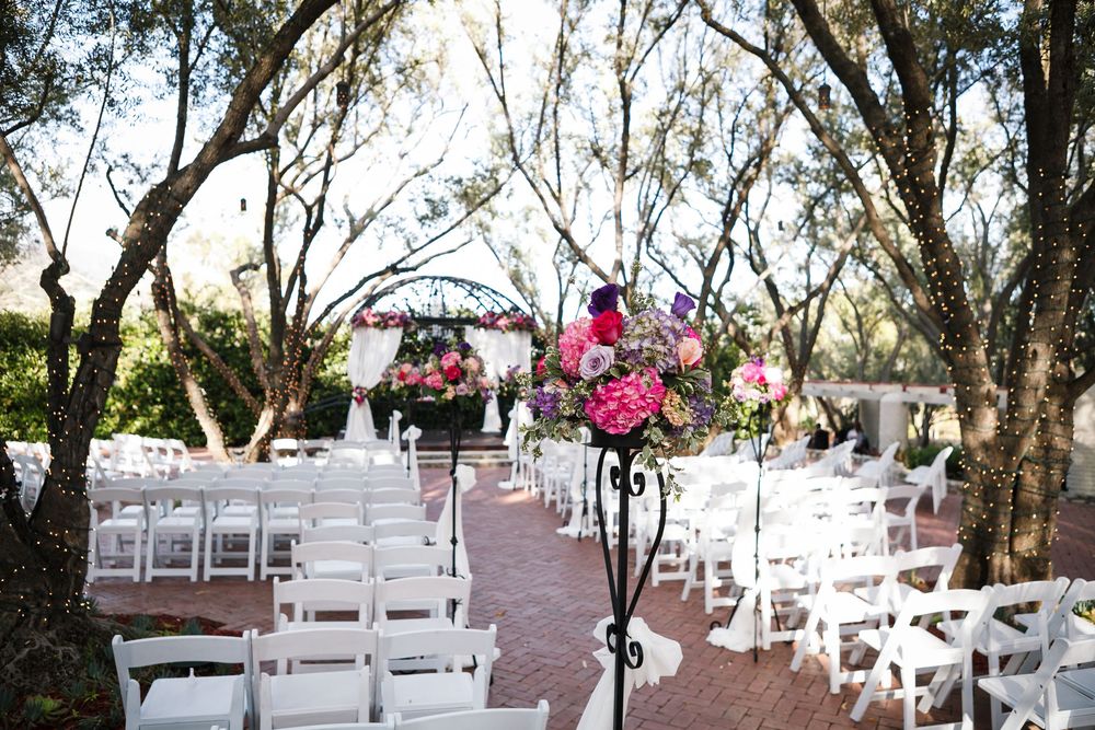 Rows of white folding chairs set up for an outdoor wedding ceremony under a canopy of trees.