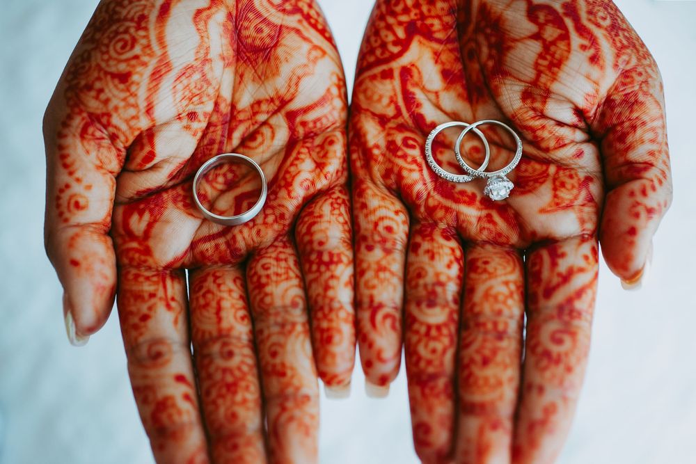 Close-up view of traditional henna mehndi designs on hands with wedding rings.