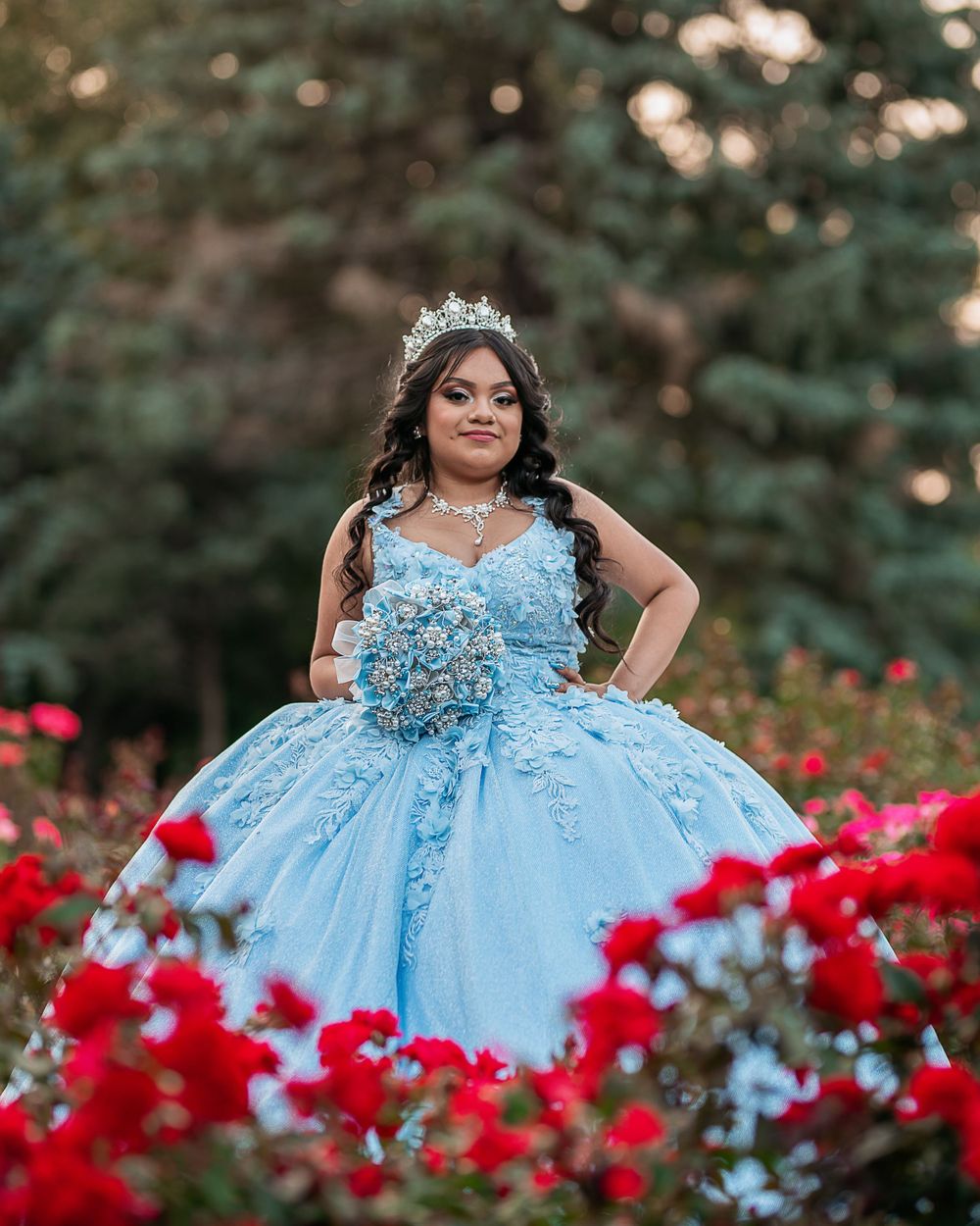 A light blue princess ball gown photographed among vibrant red flowers in a garden setting.