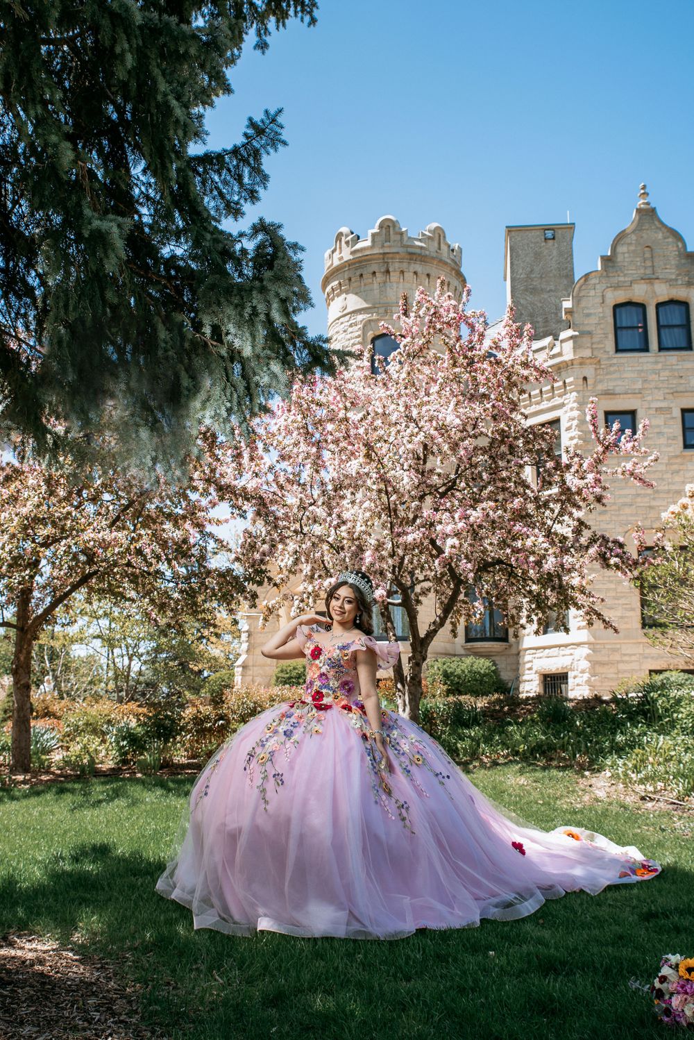 A pink princess ball gown photographed against a castle-like building with blooming trees.